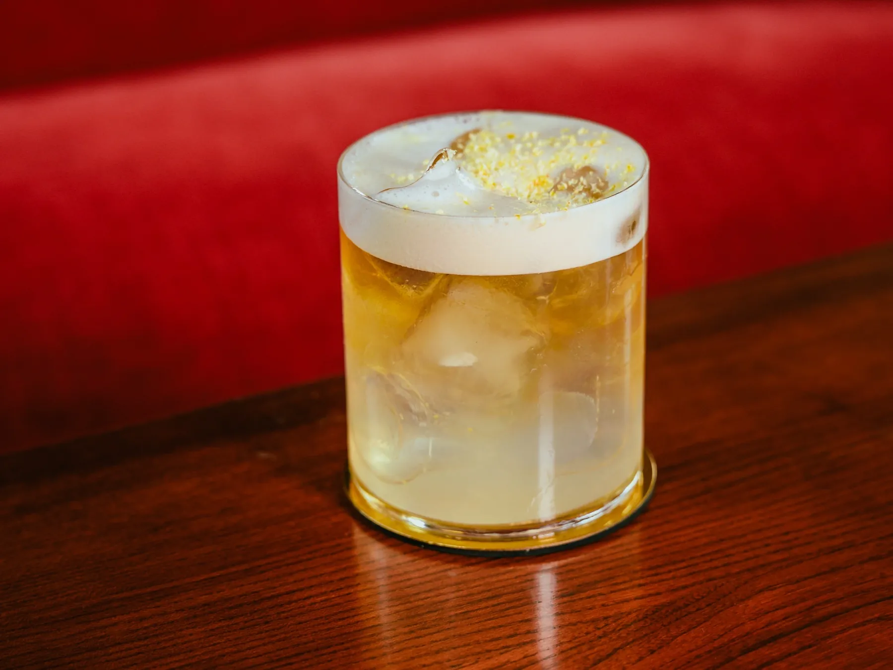 Golden Saffron Sour in un bicchiere basso con ghiaccio, la schiuma bianca compatta e una spolverata dorata sopra