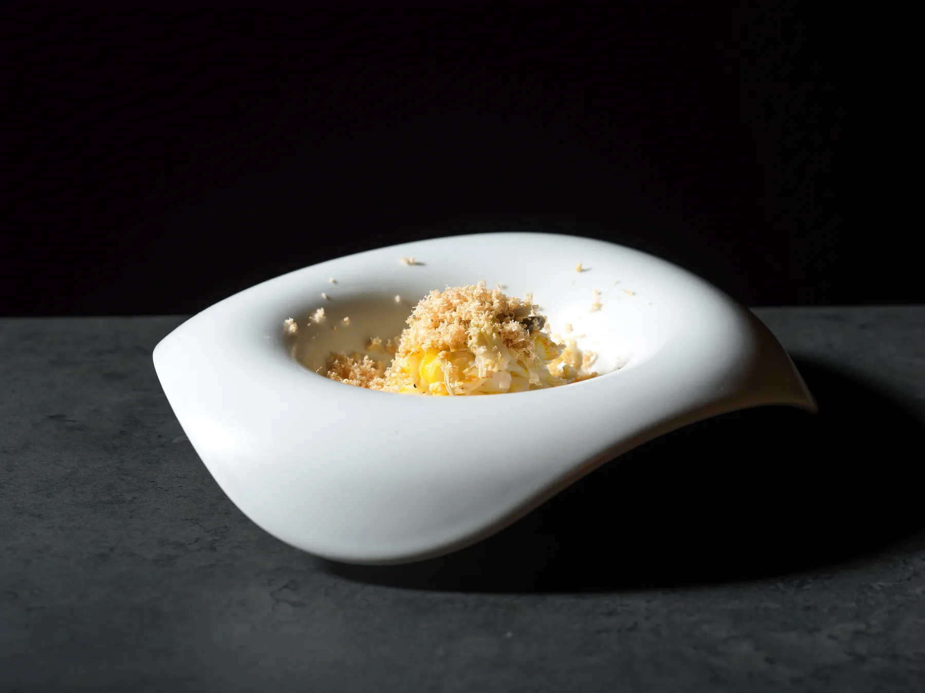 Tagliatella di seppia su bernese allo zafferano, con carciofi e Lingotto grattugiato, in una fondina bianca dal bordo ondulato