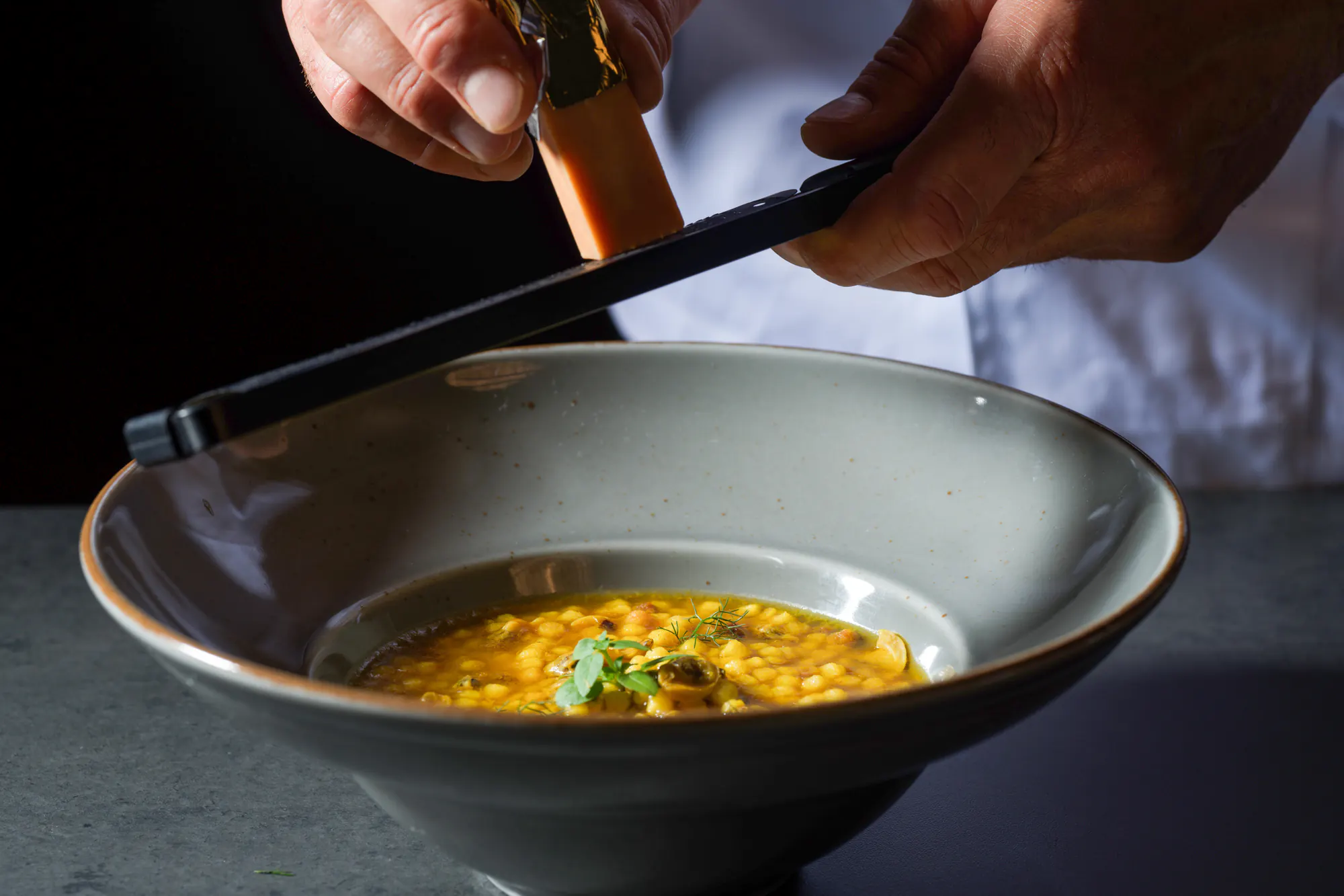 In cucina, il Lingotto grattugiato su una pasta in brodo allo zafferano, in una fondina grigia
